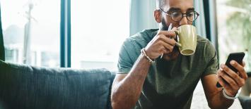 man sat on sofa drinking coffee and using facebook chatbot on his mobile