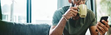 جلس رجل على أريكة يشرب القهوة ويستخدم chatbot على الفيسبوك على هاتفه المحمول
