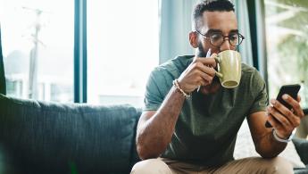 جلس رجل على أريكة يشرب القهوة ويستخدم chatbot على الفيسبوك على هاتفه المحمول