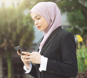 سيدة أعمال شابة ترتدي بدلة وحجاب أرجواني ، باستخدام الفرع المحمول على هاتفها