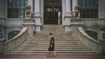 Man walking in front of official building looking at his mobile