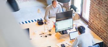 Two men sitting in an office on computers