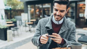 رجل يرتدي معطفاً رمادياً يستخدم هاتفه للخدمات المصرفية عبر الإنترنت
