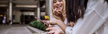 Two female friends laughing sat on a bench