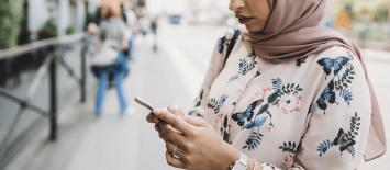 امرأة خارج ترتدي الحجاب تبحث في هاتفها المحمول